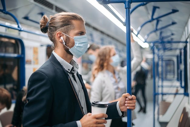 jovem com um café para viagem de pé em um vagão do metrô