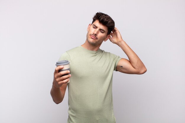 Jovem com um café se sentindo perplexo e confuso, coçando a cabeça e olhando para o lado