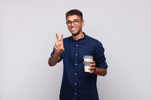 Jovem com um café sorrindo e parecendo feliz, despreocupado e positivo, gesticulando vitória ou paz com uma mão