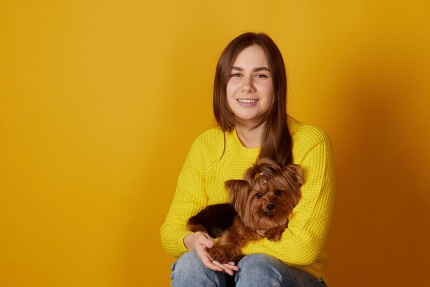 Foto jovem com um cão yorkshire terrier em um fundo amarelo limpo