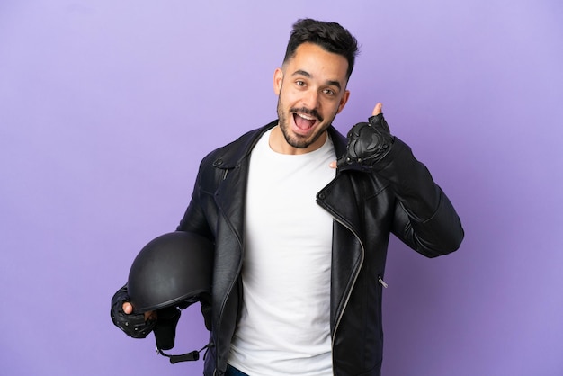 Jovem com um capacete de motocicleta isolado em um fundo roxo, fazendo gesto de telefone. Ligue-me de volta sinal