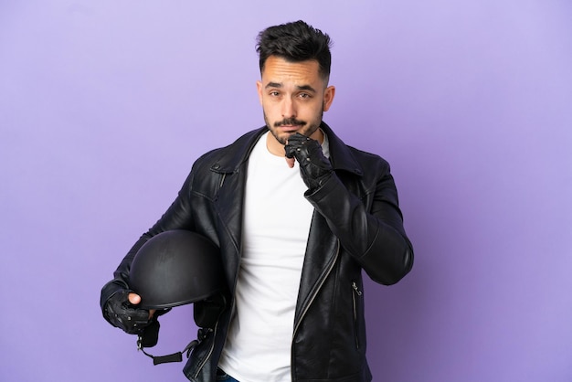 Jovem com um capacete de motociclista isolado em um fundo roxo pensando