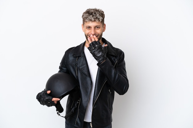 Jovem com um capacete de motociclista isolado no fundo branco feliz e sorridente cobrindo a boca com a mão