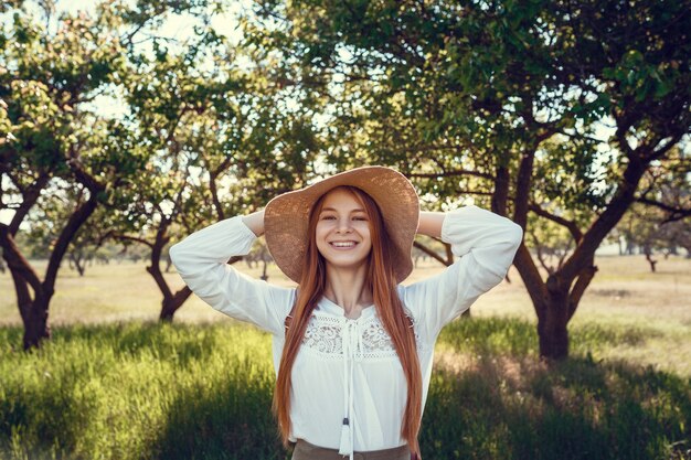 Jovem com um chapéu de palha viaja prados verdes. mulher linda ruiva hippie em um jardim verde