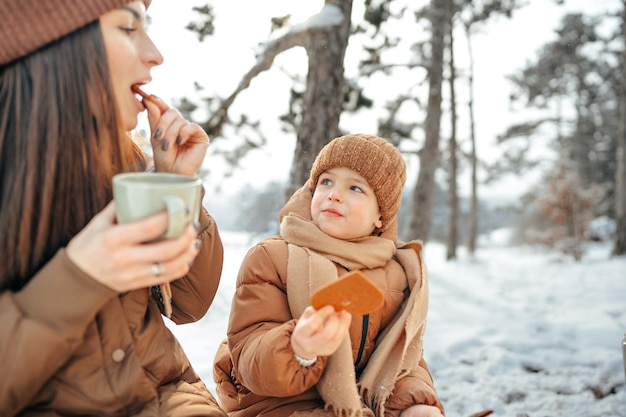 Jovem com um filho na floresta de inverno em um piquenique bebe chá quente