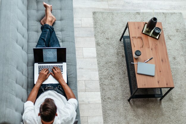 Jovem com um laptop deitado no sofá.