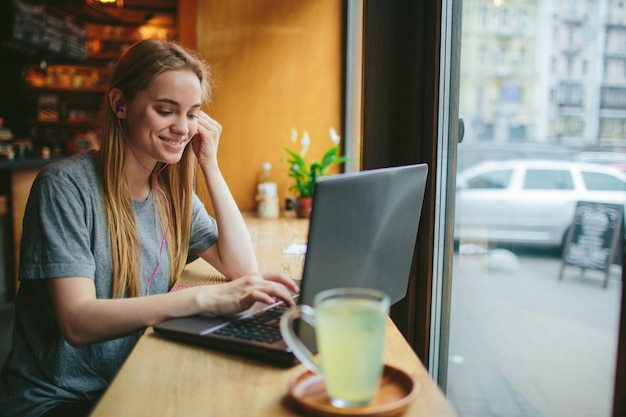 Jovem com um laptop ouve música em um café e trabalho