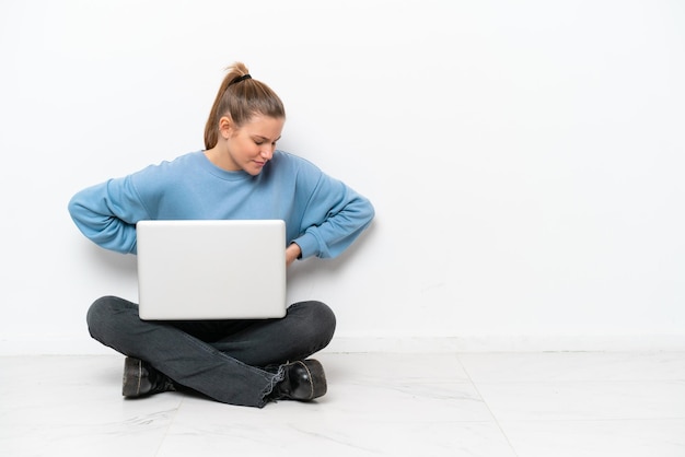 Jovem com um laptop sentado no chão sofrendo de dor nas costas por ter feito um esforço