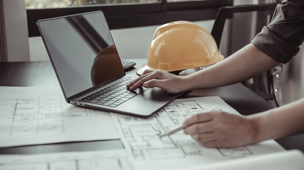 Foto jovem com um laptop traçando um sistema de estruturas de construção em planos