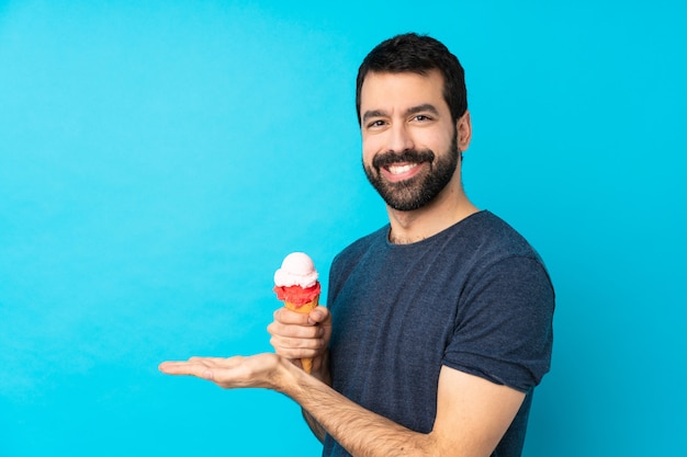 Foto jovem com um sorvete de corneta sobre parede azul isolada, apresentando uma idéia enquanto olha sorrindo para