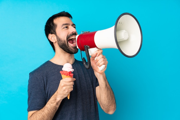 Foto jovem com um sorvete de corneta sobre parede azul isolada gritando através de um megafone