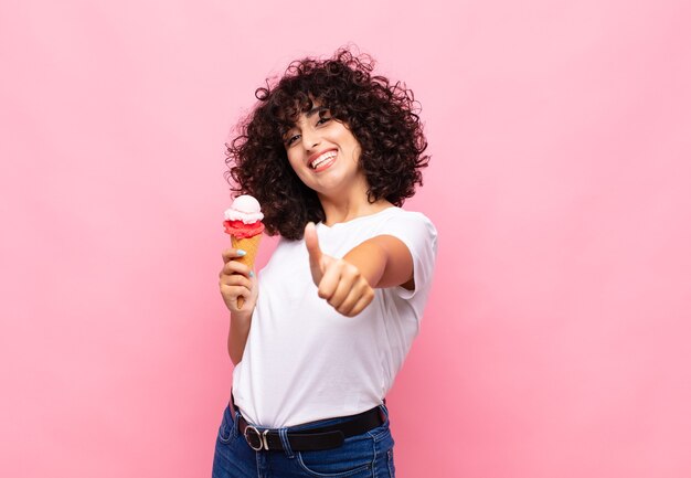 jovem com um sorvete se sentindo orgulhosa, despreocupada, confiante e feliz, sorrindo positivamente com o polegar para cima