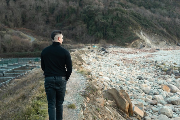 Jovem com um terno preto andando em uma praia rochosa