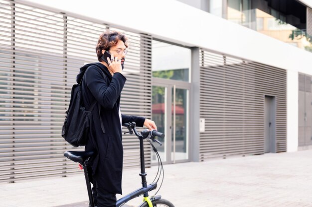 Jovem com uma bicicleta dobrável falando em seu telefone