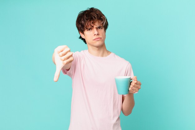 Jovem com uma caneca de café se sentindo zangado, mostrando os polegares para baixo