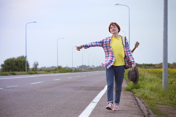 Foto jovem com uma guitarra vindo pela estrada e pedindo carona