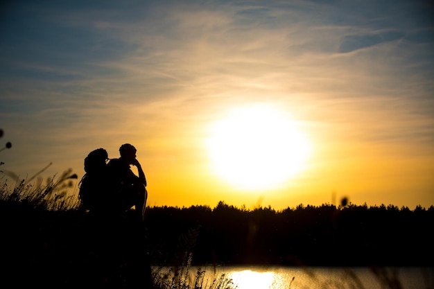 Jovem com uma mochila apreciando o pôr do sol no topo da montanha viajante turístico