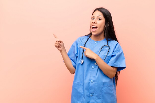 jovem com uniforme médico e estetoscópio, sentindo-se alegre e surpreso enquanto aponta para o lado