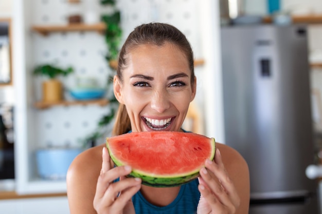 Jovem come uma fatia de melancia na cozinha retrato de jovem desfrutando de uma melancia