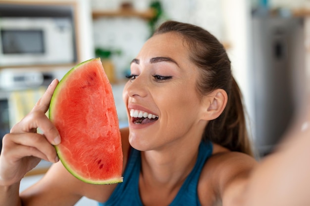 Foto jovem come uma fatia de melancia na cozinha retrato de jovem desfrutando de uma melancia