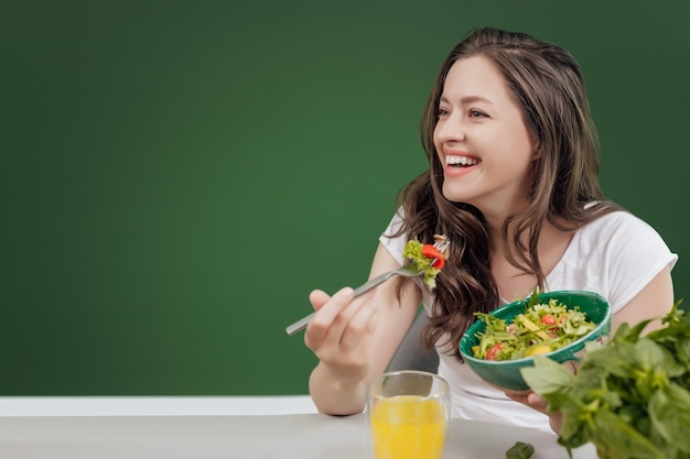 Jovem comendo comida saudável sentada no belo interior com parede verde ao fundo