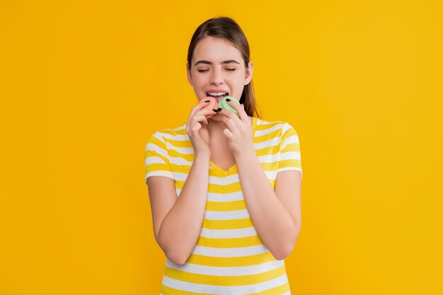 Jovem comendo macaron em fundo amarelo