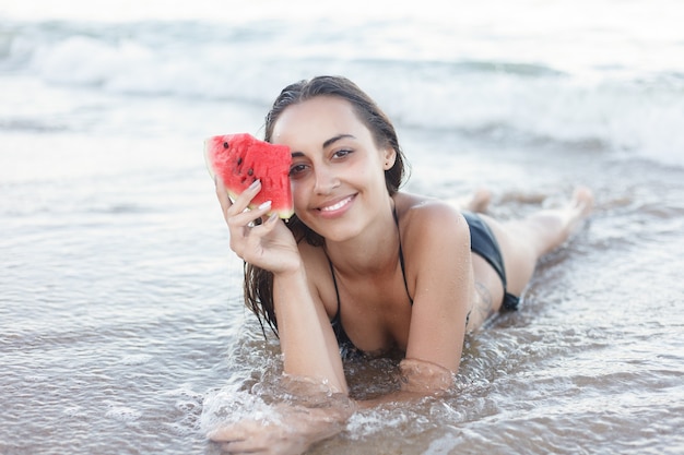 Jovem comendo melancia fresca na praia