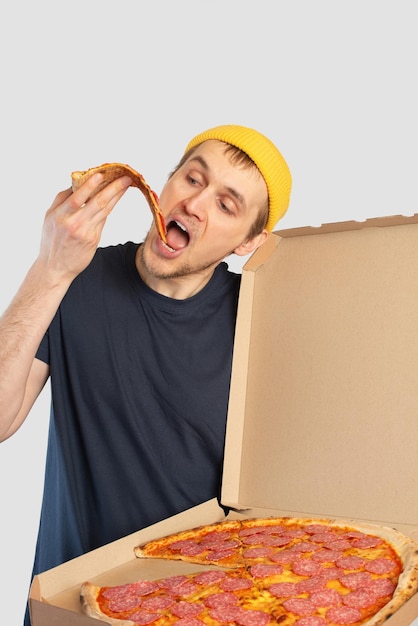 Jovem comendo pizza com uma caixa nas mãos