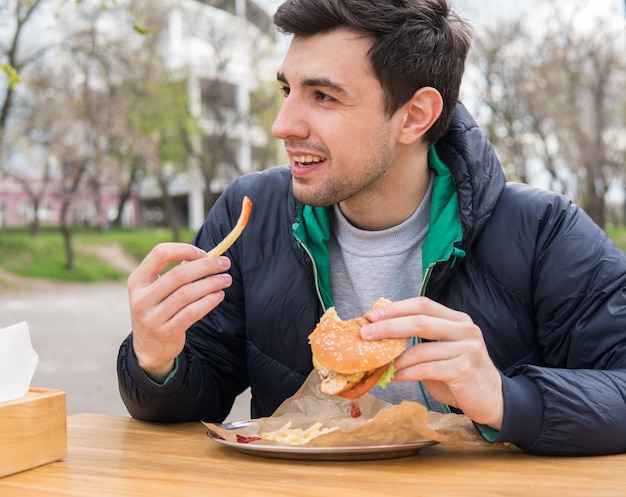 Jovem comendo um hambúrguer com batatas fritas em um café de comida de rua. Comer fast food