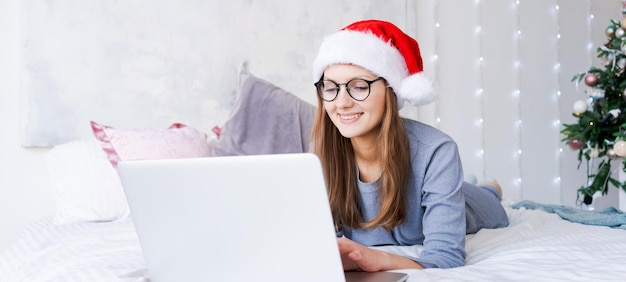 Jovem comprando on-line para o natal sente-se na cama com roupas azuis e aconchegantes