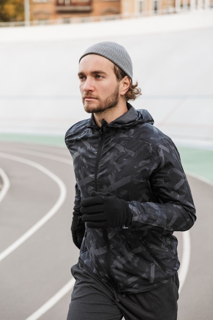 Jovem confiante em forma desportista correndo na pista de corrida ao ar livre do estádio