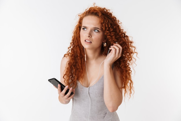 Foto jovem confuso incerto ruiva encaracolado mulher usando telefone celular ouvindo música.