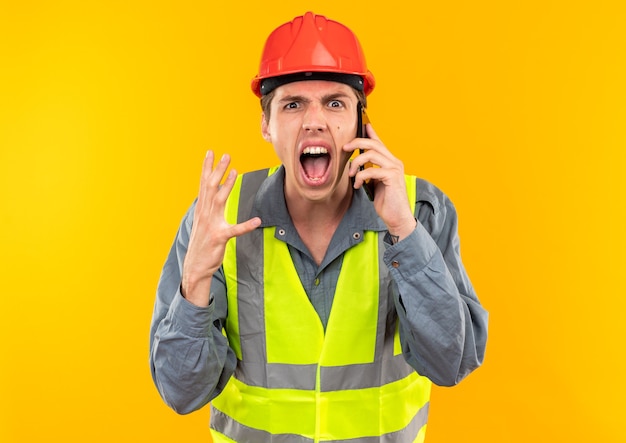 Jovem construtor de uniforme furioso falando ao telefone