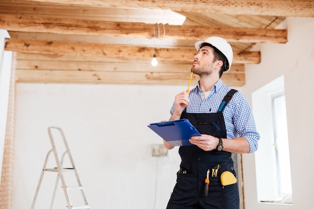 Jovem construtor especialista pensativo examina seu espaço de trabalho