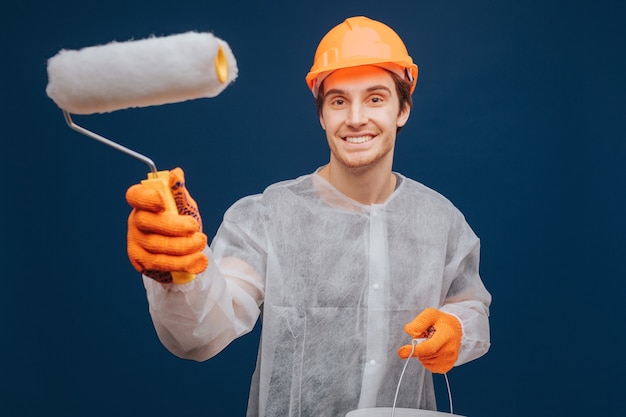 Jovem construtor está segurando o rolo para pintar a parede e sorrir