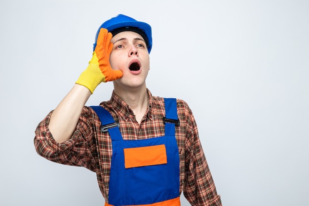 Jovem construtor usando uniforme com luvas isoladas na parede branca