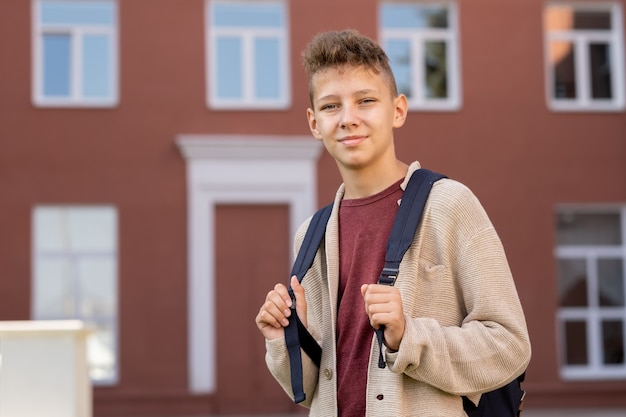 Jovem contemporâneo com mochila encostada na parte externa do prédio