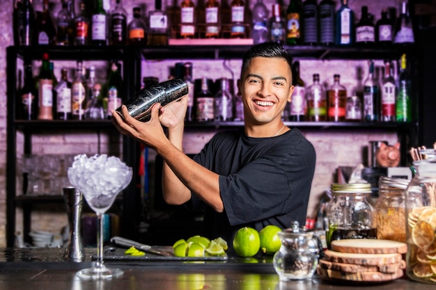 Jovem coqueteleira sorridente agita uma coqueteleira atrás de um bar do clube, olhando para a câmera