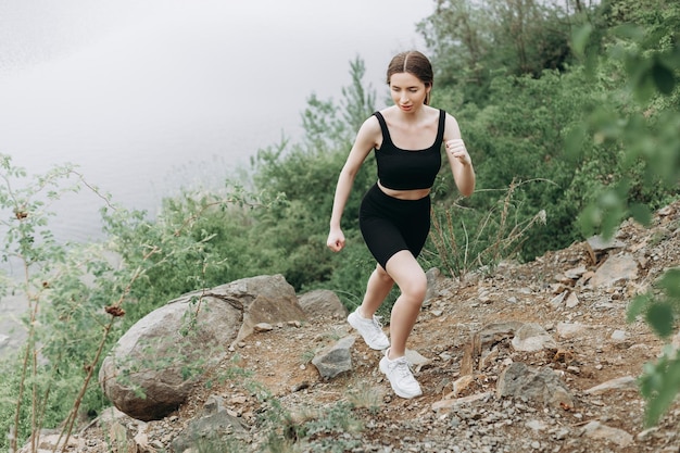 Jovem corredora esticando braços e pernas antes de correr na trilha da floresta matinal perto do lago