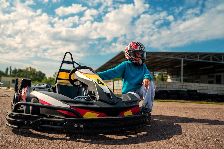 Foto jovem corredora posando perto de um carro de corrida de karting na pista usando um capacete em um dia ensolarado claro