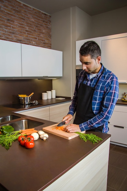 Jovem cortando vegetais na cozinha para preparar comida