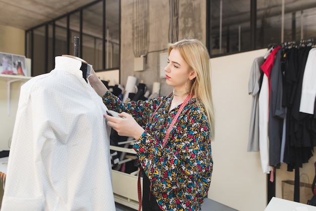 Jovem costureira feminina fica em um estúdio bem cuidado e ajusta as roupas.