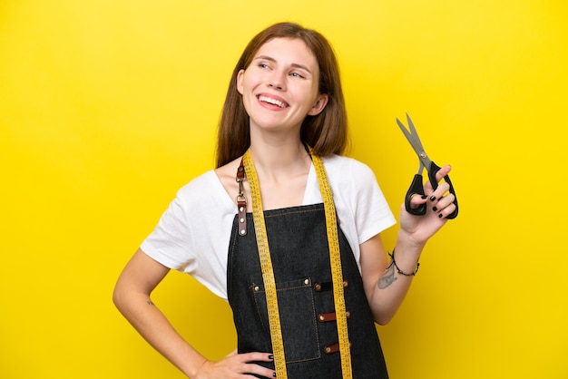 Jovem costureira inglesa isolada em fundo amarelo posando com braços no quadril e sorrindo