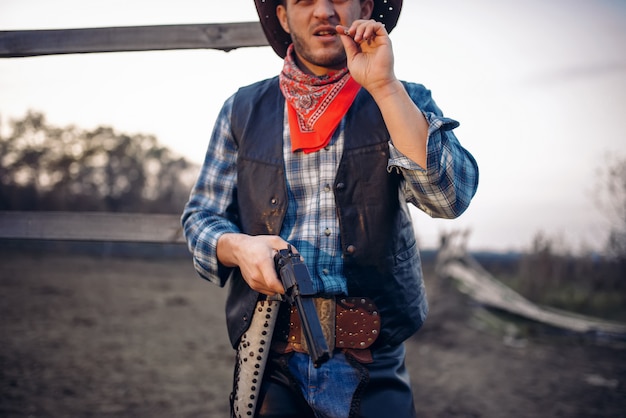 Jovem cowboy com poses de arma contra curral de cavalos