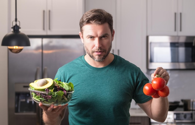 Jovem cozinhando salada vegana saudável na cozinha homem milenar na mesa da cozinha moderna cortar vegetais