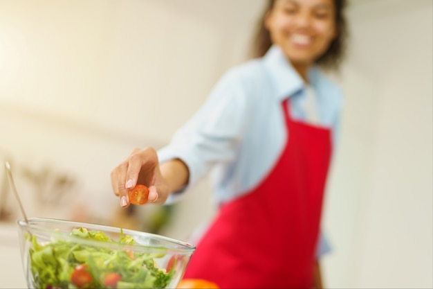 Jovem cozinheira com avental a preparar uma salada na cozinha