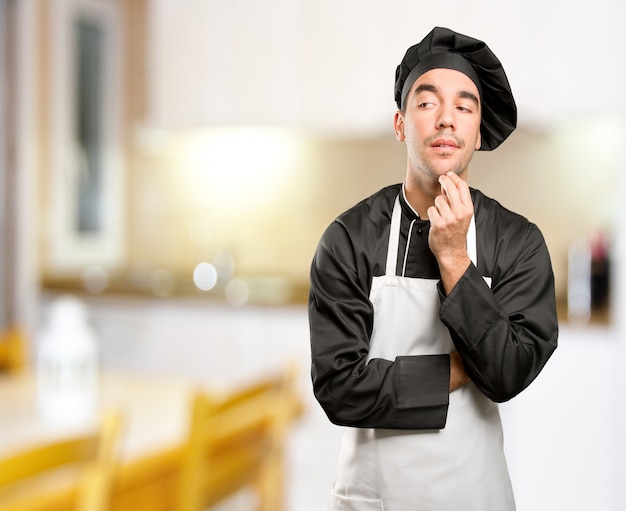 Jovem cozinheiro feliz duvidando