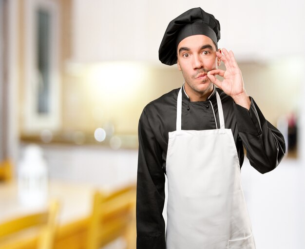 Jovem cozinheiro feliz fazendo um gesto de silêncio