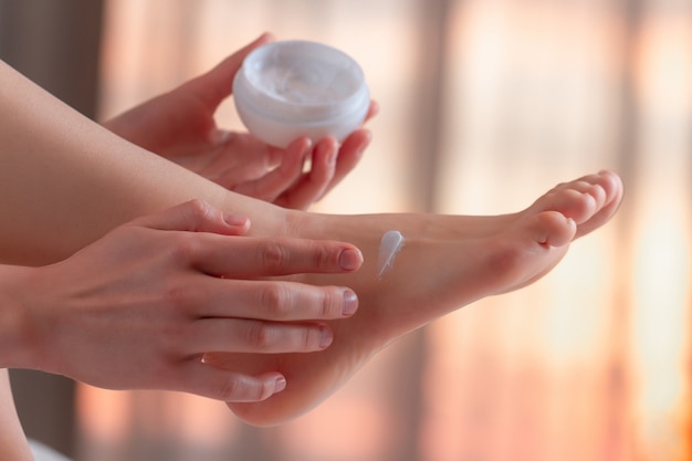 Jovem cuidando dos pés e aplicando creme hidratante e hidratante. cuidados com os pés e a pele.