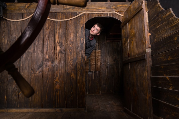 Jovem curioso homem de negócios espiando por dentro da porta da cabine de um antigo veleiro de madeira